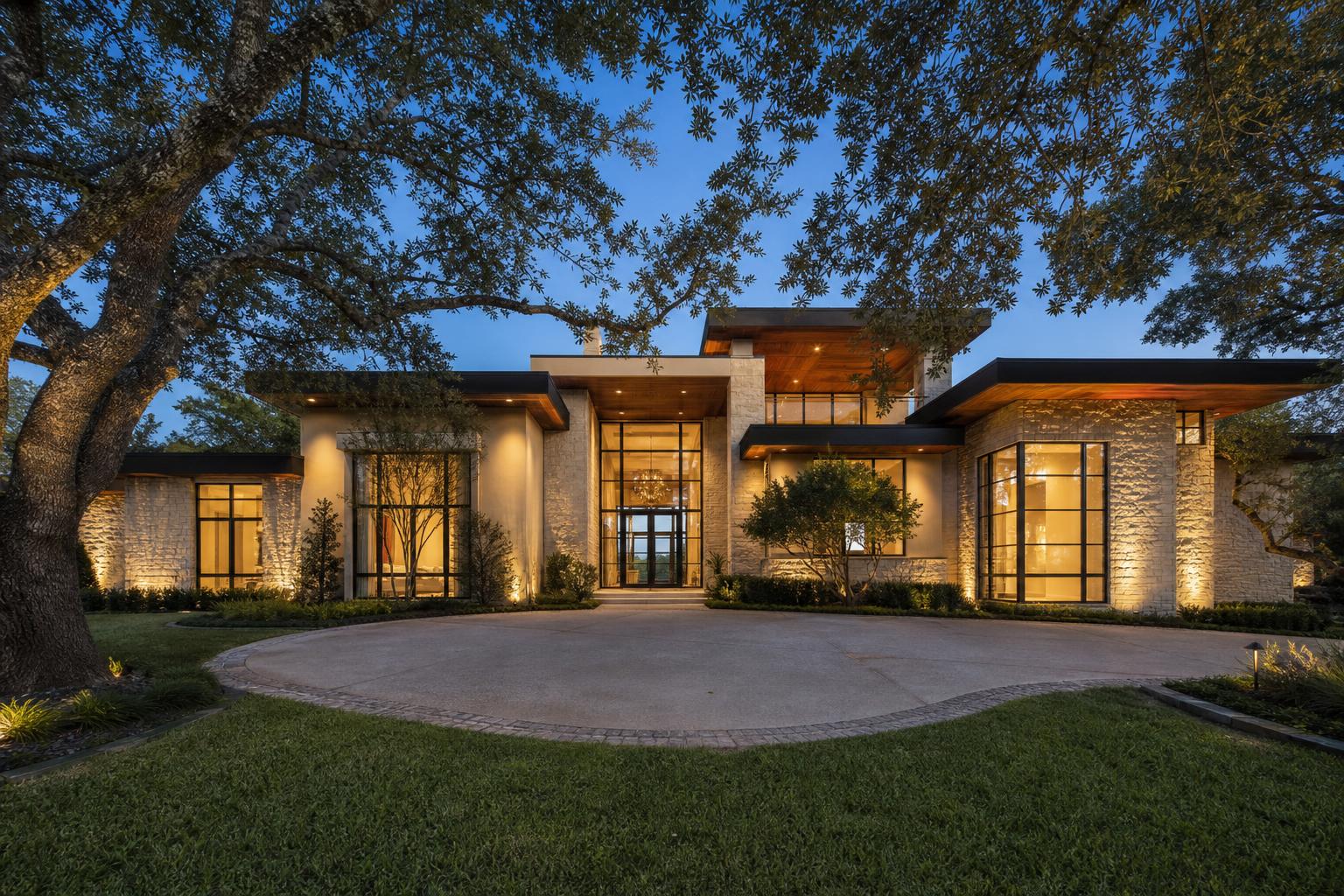 Modern Highland Park limestone and stucco home exterior at dusk with live oak trees