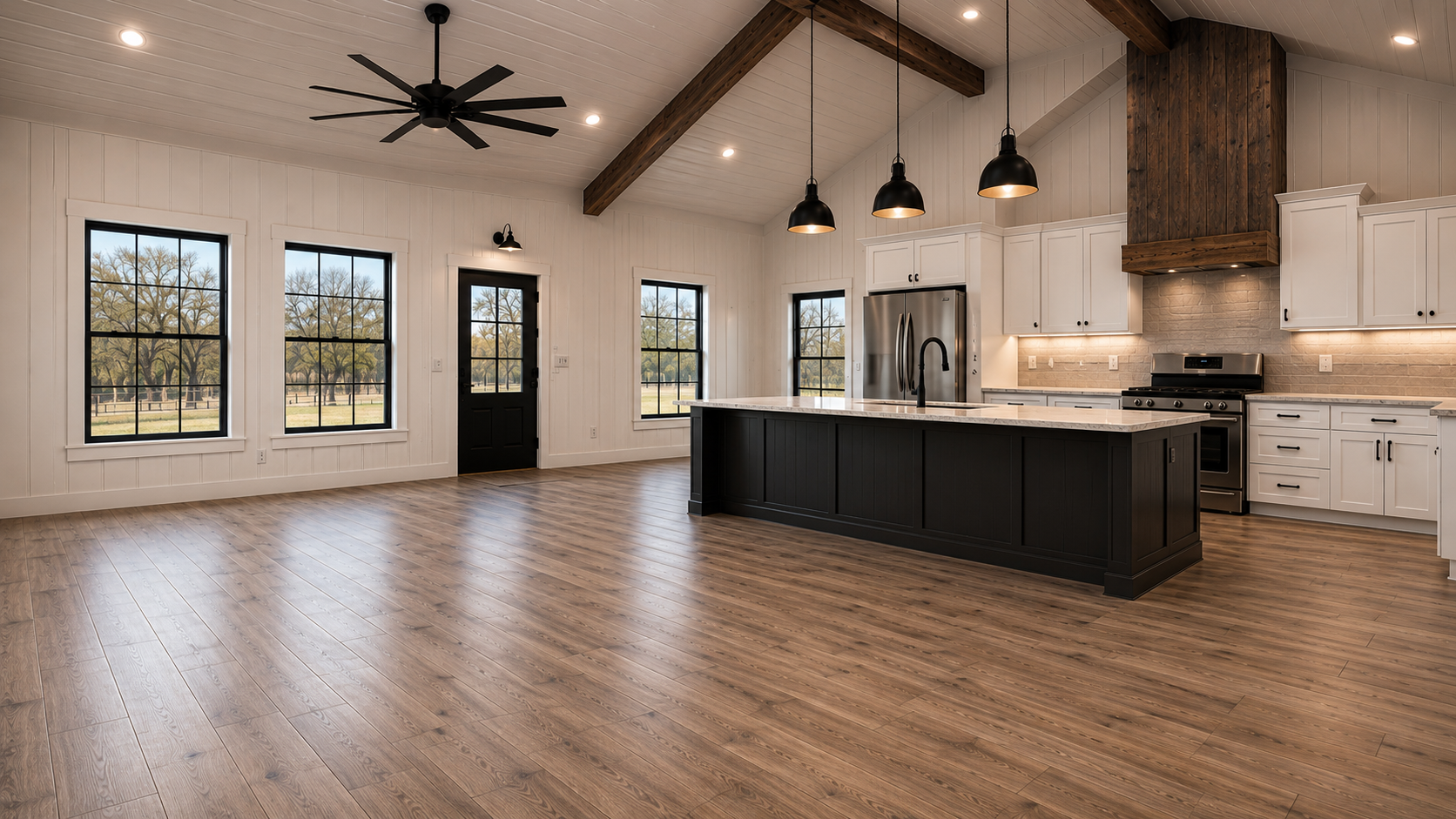 Open concept barndominium great room and kitchen with vaulted shiplap ceiling, wood beams, black island and farmhouse windows