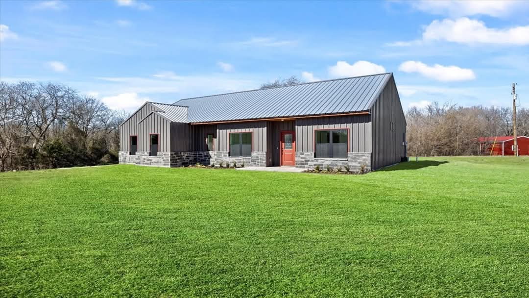 Dark gray board-and-batten barndominium with standing seam metal roof and stone accents